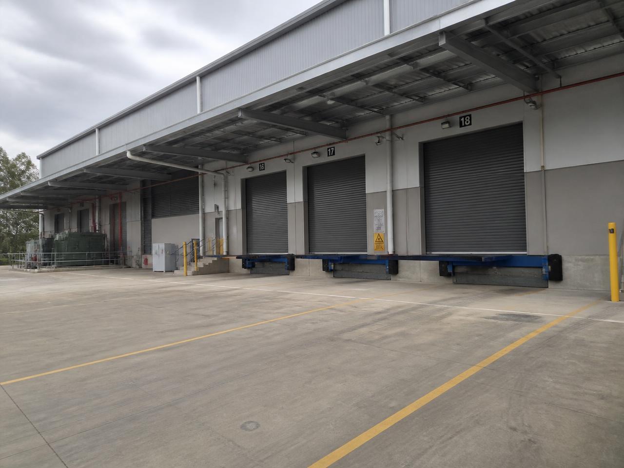 Loading dock area of an industrial commercial asset in use, with roller doors, dock levellers and line-marked hardstand.