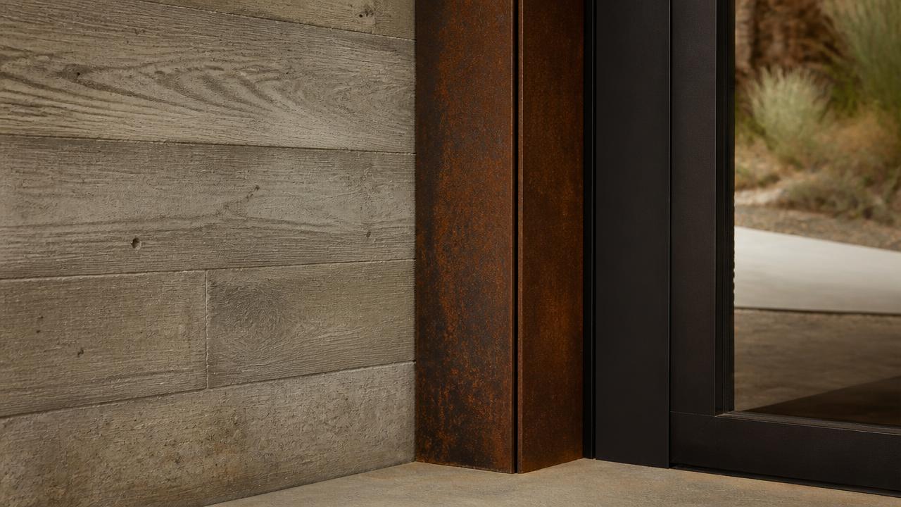 Board-formed concrete wall meeting a weathered steel column base at the entry of a commercial building.
